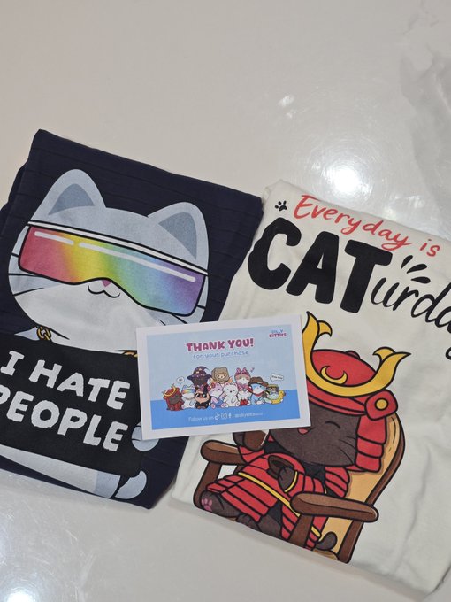 Two cat-themed t-shirts are displayed alongside a "THANK YOU! For your purchase" card from "Crypto Kitties," one shirt featuring a cat in rainbow sunglasses with the text "I HATE PEOPLE" and the other reading "Everyday is CATurday" with a samurai cat design, echoing the post's grateful shoutout to @kookoocryptotv and the playful "Stay Silly" spirit.