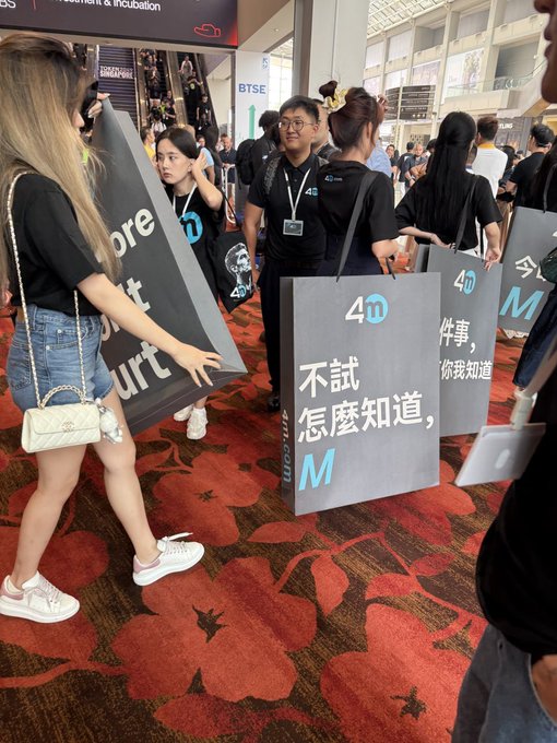 People carry large grey signs with Chinese text at what appears to be a conference, with one sign reading '不試怎麼知道' (How would you know if you don't try).