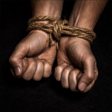 Two clenched hands bound together tightly with rough rope against a black background, symbolizing captivity or restraint.
