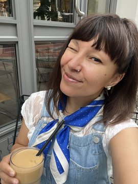 A woman winks while holding an iced coffee, wearing a blue and white scarf printed with the WalletConnect logo to match the post about using crypto through WalletConnect to save her coffee date.