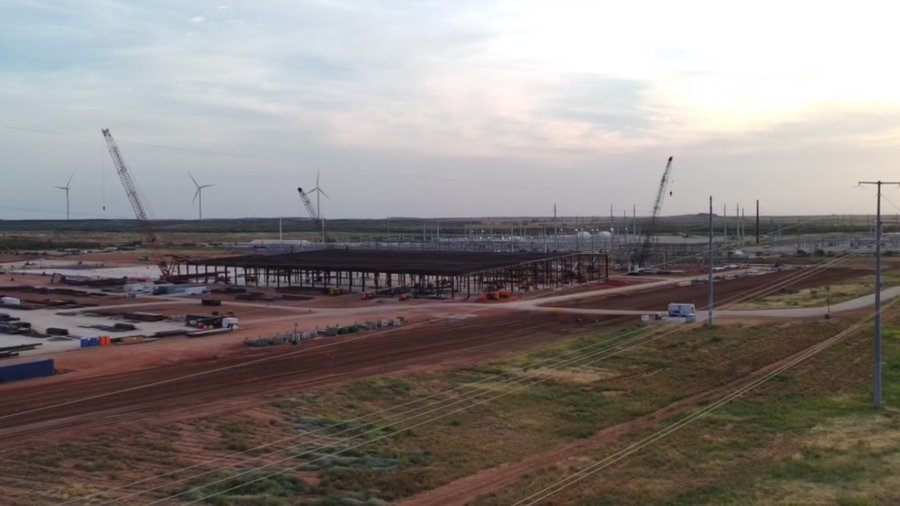 An expansive industrial construction site featuring cranes, a large steel-framed structure, and wind turbines in the background, depicting the ongoing development of IREN's Childress facility (SW1) in West Texas, with earnings scheduled for January 27th.