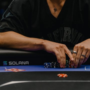 A player arranges chips at a poker table featuring "SOLANA" branding on the felt, in preparation for the WSOP x Solana tournament with a $100,000 prize pool among nine online competitors. The image captures the tense, focused moment before gameplay begins, visually reflecting the post's excitement about the high-stakes, online crossover tournament.