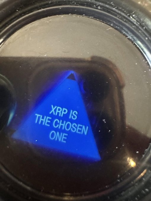 A close-up of a smartwatch screen displays a blue pyramid graphic with the text "XRP IS THE CHOSEN ONE." The image humorously ties into the post's bewildered reaction at XRP's apparent rise to crypto dominance, framing the cryptocurrency's ascent as some sort of destined prophecy.