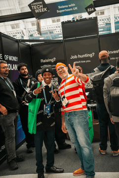 The image shows a group of people standing next to each other at an event related to job hunting, possibly an expo or convention. One man stands out, holding up his hand with both fingers showing, smiling widely as he poses for a picture. The rest of the attendees in the background are looking on and participating in various activities within their surroundings. There is also a text post that reads "WINNERS FOUND WALLY HERE'S everything they won over the last 3 days @LDN tech week: 100+ Solana & #superteam stickers 80+ Solana merch (tshirts, hoodies, beanies, caps) 50+ PS5". This post likely contains information or announcements related to the job hunting event being held in the scene.