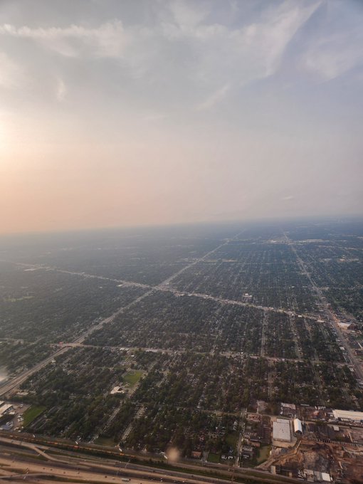 Aerial view of a sprawling suburban landscape with a grid-pattern street layout extending to the horizon under a hazy sky.