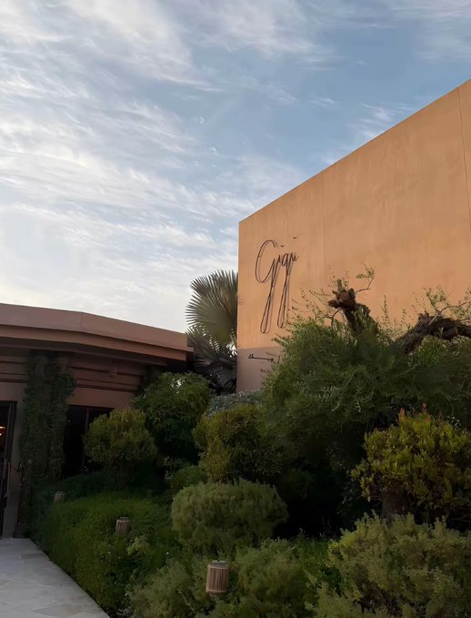 An exterior view of a building with tan walls and greenery, with cursive signage partially visible reading 'Grill' at sunset.