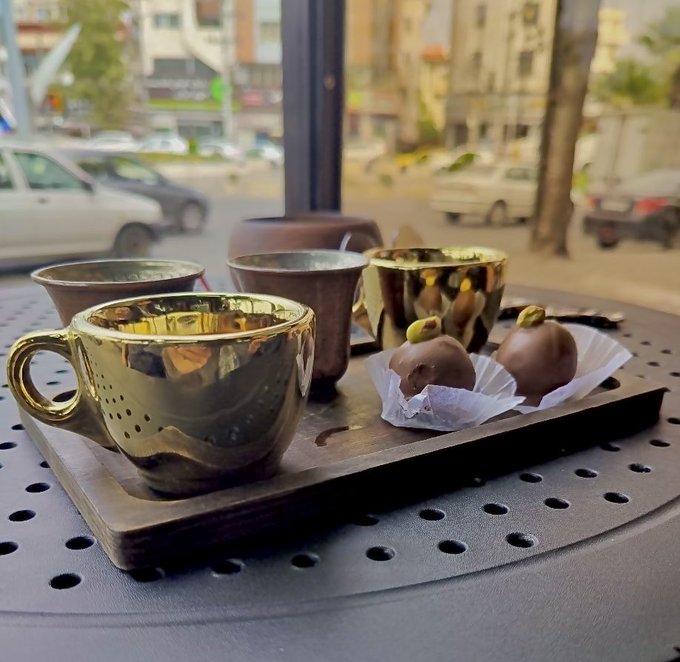 A street-side tray holds ornate gold-colored cups and two chocolate-covered confections, with parked vehicles and buildings blurred in the background.