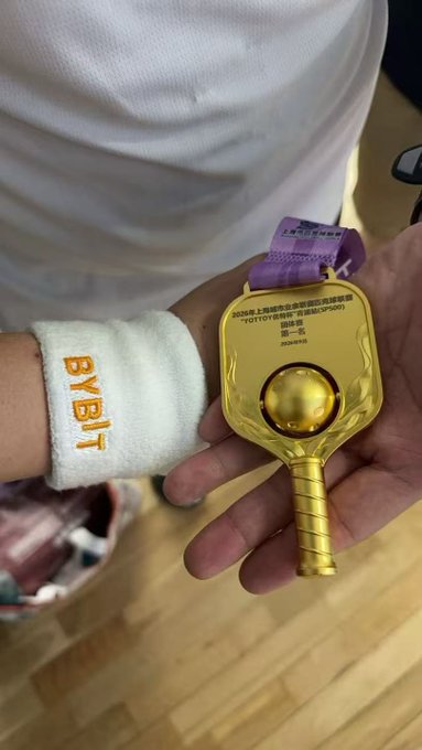 A person holding a golden key-shaped medal or trophy with a purple ribbon; the medal reads '2026年上海市运动会 (SOCOG系列赛事) TOTO定向越野锦标赛 决赛·组一名' indicating a first-place finish.
