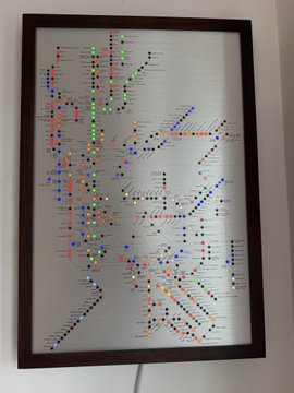 A framed subway/transit map poster on a wall, decorated with colorful magnetic pins marking various station locations along the colored lines.