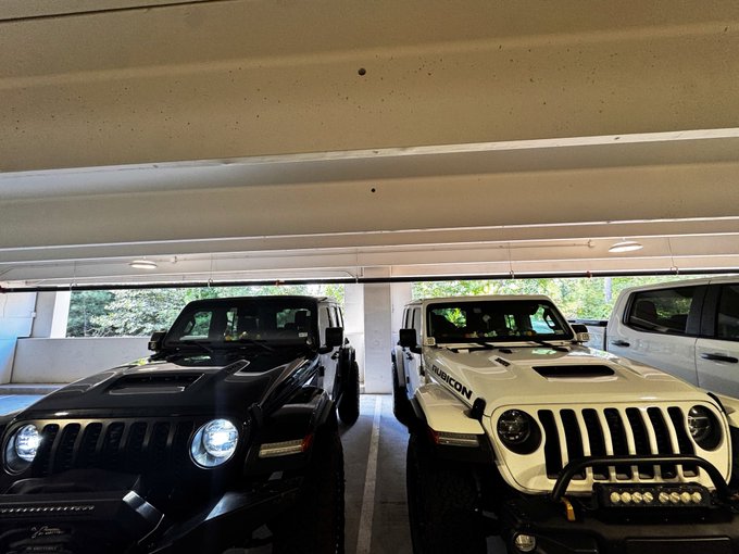 Two Jeep vehicles, one black and one white with 'RUBICON' branding, are parked side by side in an indoor parking garage.