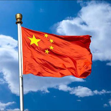 The flag of the People's Republic of China, red with five yellow stars, waving on a flagpole against a blue sky with white clouds.