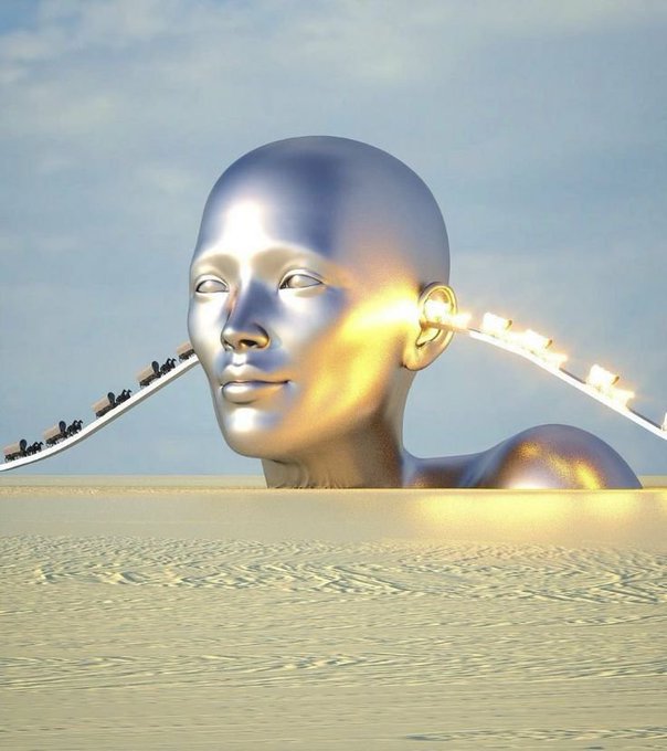 A 3D-rendered surreal scene of a large, metallic silver human head emerging from a sandy desert, with a glowing roller coaster track looping through its ear area.