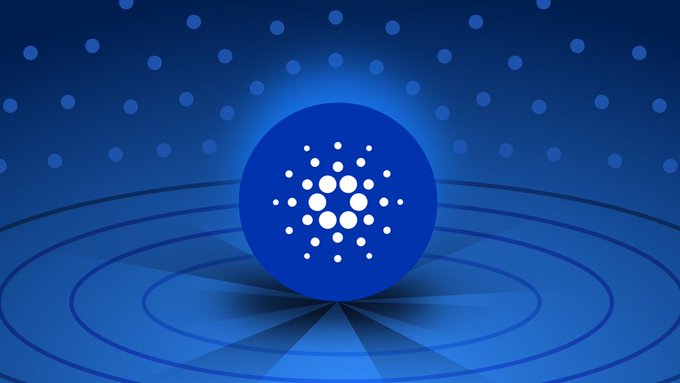 A blue Cardano coin logo featuring a white dot cluster pattern, displayed prominently against a blue background with circular ring patterns and scattered dots.