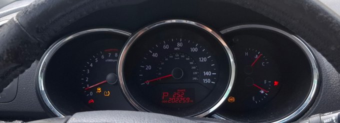 A close-up photograph of a vehicle's instrument cluster showing the speedometer, tachometer, and fuel/temperature gauges, with multiple warning lights illuminated (including check engine, airbag, and seatbelt indicators) and the odometer reading 138269 miles.