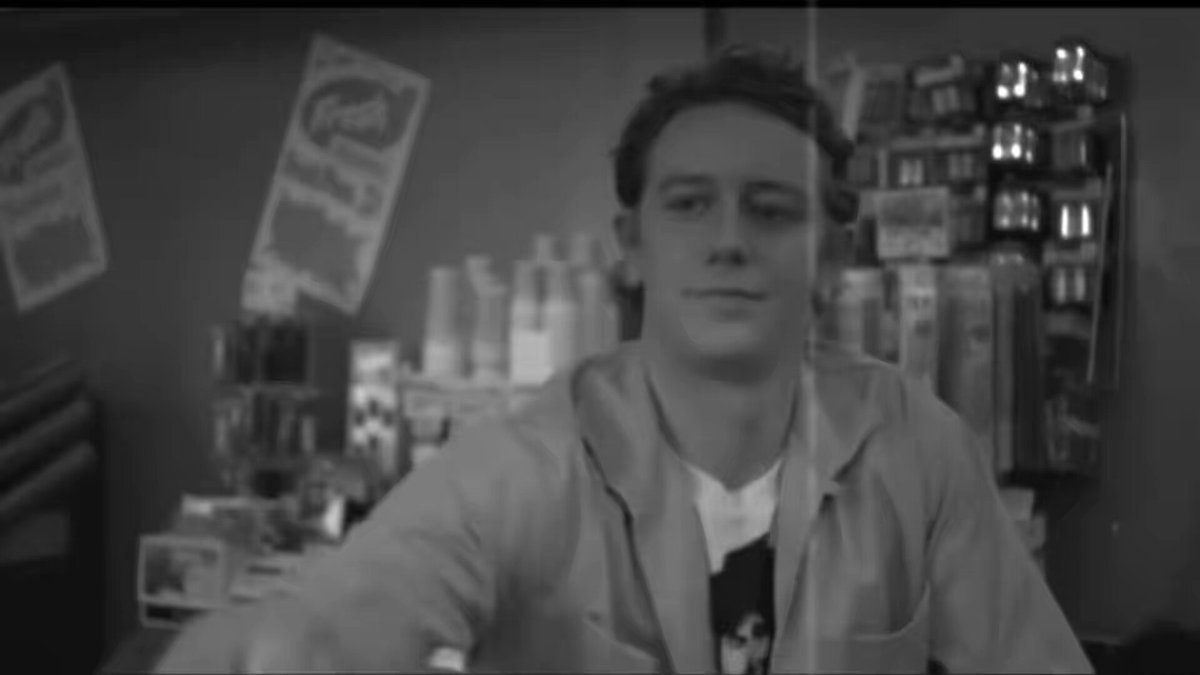 The image features a young man wearing a white shirt, sitting at a counter with his arm outstretched as if he's about to make a gesture or gesture towards someone. The background of the image shows various items such as bottles and posters on the wall behind him. There is also an accompanying text that reads "Spicoli is unemployed...be like Spicoli live the $neet life". This suggests that the young man in the image might be making a playful or humorous gesture, possibly referencing the character Spicoli from the movie "The Godfather" who was known for his love of spicy food.
