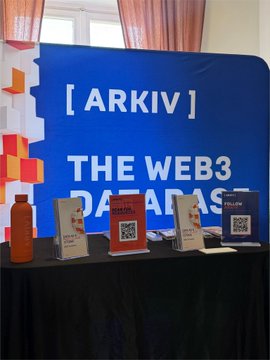 An ARKIV booth banner reads '[ ARKIV ] THE WEB3 PARADISE' with informational cards and a water bottle on a table below.