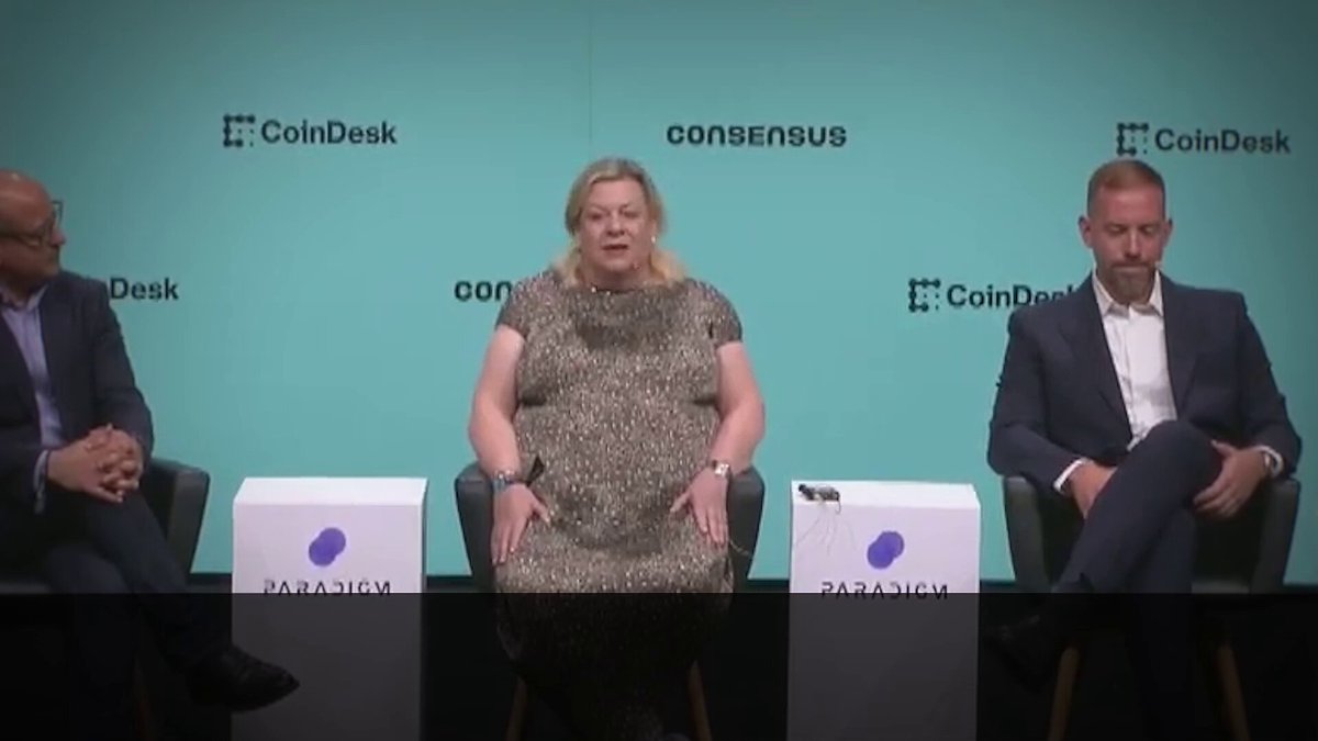 The image shows three people sitting at a table, with two men wearing suits and one woman wearing a dress. They are all facing the camera, appearing engaged in conversation or discussion. The backdrop features a blue wall with white text that reads "CoinDesk" and "Regulatory tailwinds and increasing public market education will help usher in the next wave of on-chain economies." This suggests that they might be discussing the current state of cryptocurrency regulation and its potential impact on the future of digital assets.