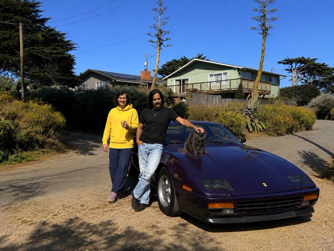 A couple poses with their purple Ferrari sports car in front of a coastal home with a black cat perched on the hood, while the accompanying post references $FIDEL as a notable cat, drawing a playful parallel between the feline in the photo and the cryptocurrency they favor.