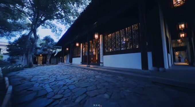 A twilight scene of a traditional Chinese building with glowing lanterns, featuring a stone-paved path leading past white walls and dark wooden lattice windows.