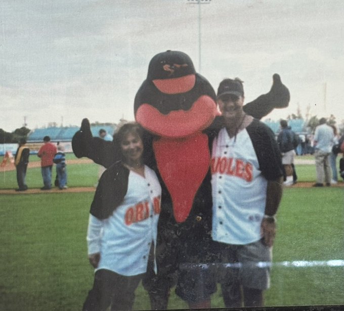 An old photograph of a couple wearing Baltimore Orioles jerseys posing with the Oriole Bird mascot at a baseball stadium.