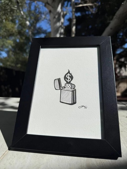 A framed minimalist black and white line drawing of a lighter with a flame shaped like a dollar sign, sitting outdoors on a table.