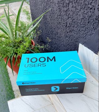 The image shows a cyan and black cake decorated with "100M USERS" and "Bitget Wallet" branding, complete with candle iconography, celebrating the milestone mentioned in the post.
