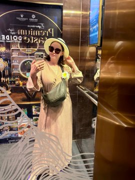 A woman in a beige dress and straw hat takes a mirror selfie inside an elevator, with a 'Pricing Project' advertisement visible behind her.