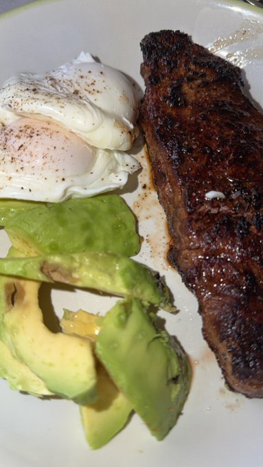 A close-up photo of a breakfast plate featuring a well-seared steak, two poached eggs sprinkled with pepper, and sliced avocado.