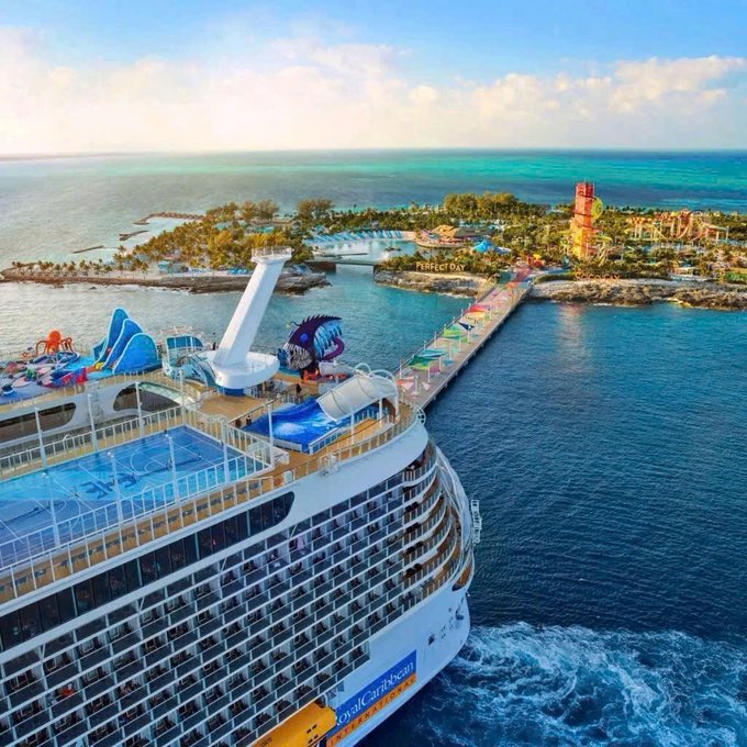 An aerial view shows a Royal Caribbean cruise ship docked at Perfect Day at CocoCay, featuring a water park and lighthouse.