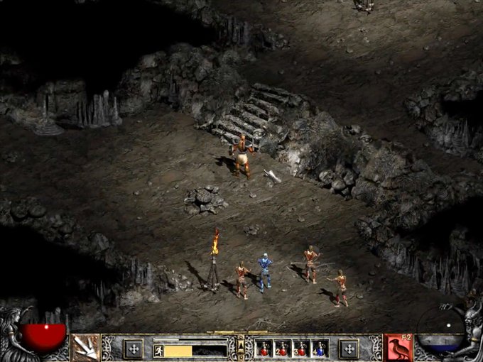 A screenshot from the video game Diablo, showing a character exploring a dark cave with skeletal remains, accompanied by a group of followers near a torch.