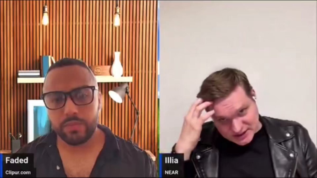 The image shows two men having a conversation over video chat. One man has his hand up to his head, while the other man looks at him with interest or concern. The background of the image features a wooden wall with several books on shelves behind them.
