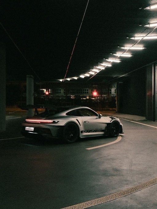 A grey Porsche 911 GT3 RS with a large rear wing driving through a dimly lit parking garage.