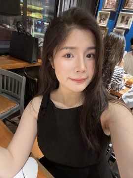 A selfie of a young woman with long dark hair wearing a black tank top in a restaurant setting.