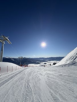 A bright sunny day on a snow-covered ski slope with chairlifts visible under a clear deep blue sky.