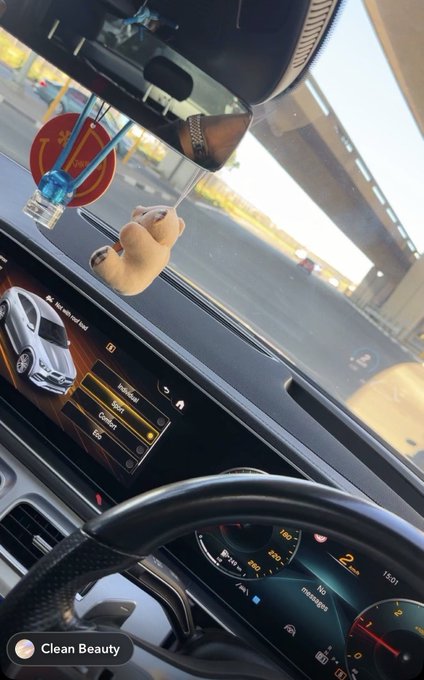 A first-person view from inside a car, showing a hand holding a straw towards the dashboard, with the car's infotainment screen visible and an Instagram story tag "Clean Beauty".