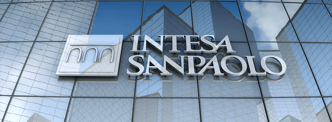 The exterior of a modern glass building displays a large silver sign reading 'INTESA SANPAOLO' with the company's logo to the left.