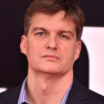 A close-up headshot of a serious-looking middle-aged man with brown hair, wearing a dark pinstripe suit jacket over a light blue striped shirt, likely Michael Burry referenced in the post about his AI bubble warning.