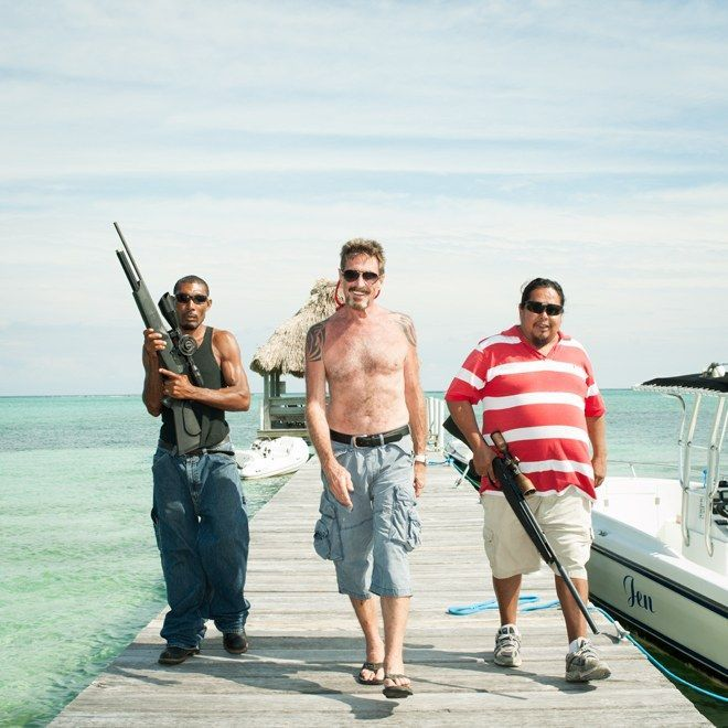 Three men standing on a wooden dock by the ocean, with the two men on the sides holding shotguns and the shirtless man in the middle wearing sunglasses.