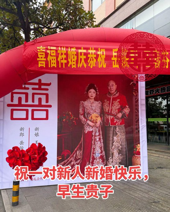 A traditional Chinese wedding photo display featuring a couple in red traditional attire, with banners reading '幸福祥婚庆恭祝' and '祝一对新人新婚快乐, 早生贵子' (wishing the newlyweds a happy marriage and early blessing of children).