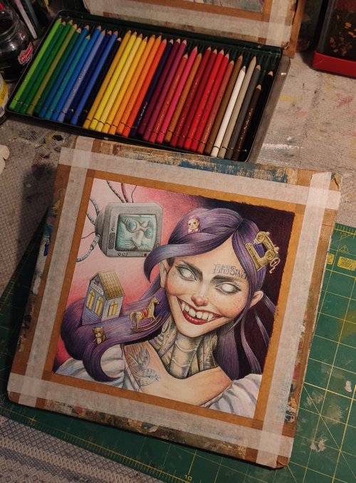 A completed colored pencil portrait of a tattooed woman with purple hair, a wide smile, and surreal floating elements sits taped to a board, with a tin of colored pencils above it.