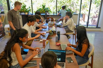 Hackers at the Startup School Hackathon collaborate on laptops at a shared table, embodying the collaborative spirit of building AI agents that need a built-in wallet to transact and pay for services autonomously.