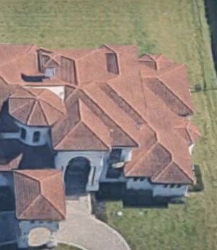 An aerial view of a large luxury mansion featuring an intricate multi-tiered terracotta tile roof, set on a sprawling green lawn.