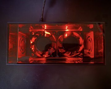 An illuminated decorative lamp made from a transparent cassette tape with red LED lights glowing inside, casting a warm red glow against a dark background.