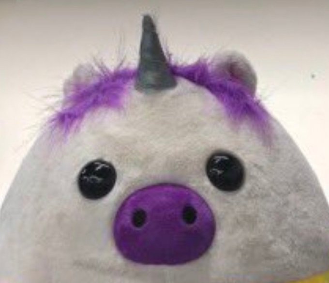 A close-up of a plush unicorn toy featuring white fur, a gray horn, black eyes, and purple accents on its cheeks and ears.