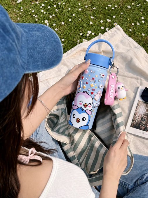 A person wearing a blue denim bucket hat holds a light blue water bottle decorated with cute penguin characters and a 'FOLLV' tag, sitting on a striped picnic blanket.