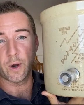 A man holds up a ceramic jug labeled "Naturally Occurring Radioactive Ore Remedy" with text referencing "BURN" and drinking instructions, displaying the container of radioactive water he claims to consume daily as part of his alternative health regimen.