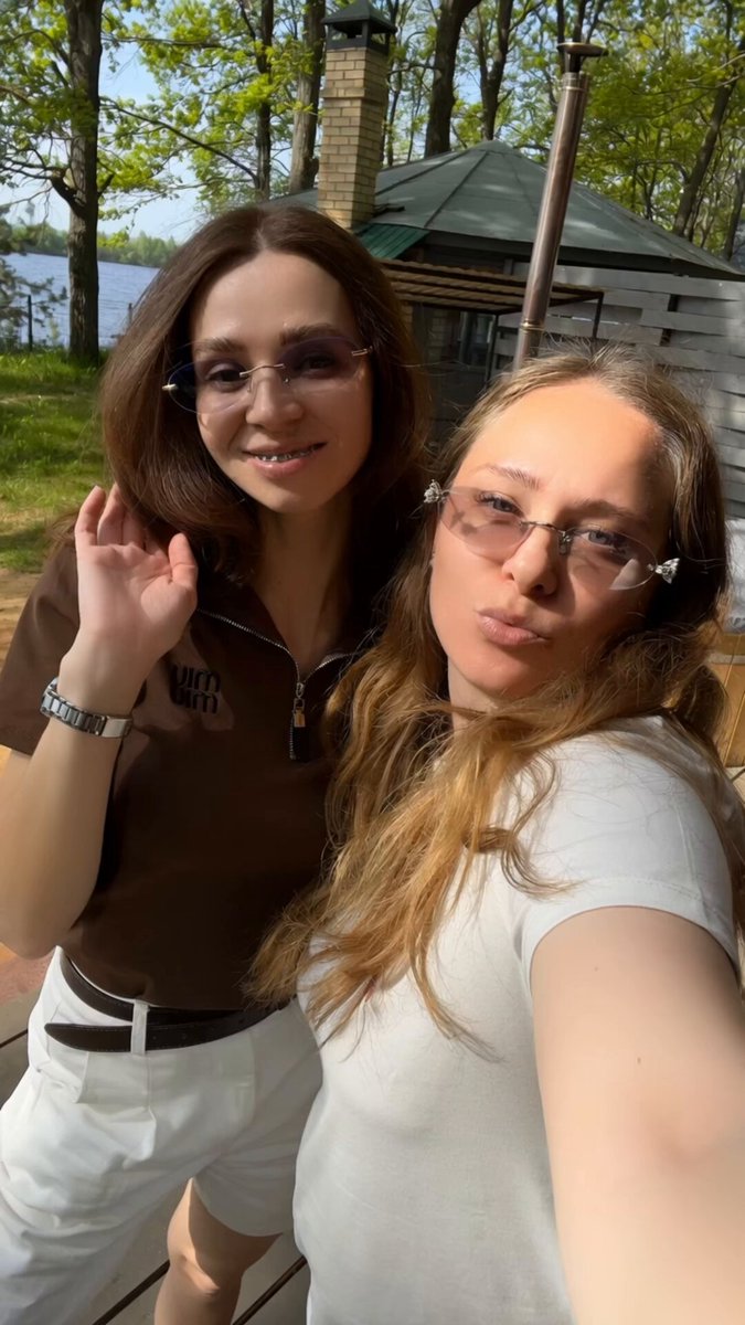 The image features two women standing next to each other outdoors, both wearing glasses and smiling for a photo. They are positioned near a building with a chimney, suggesting that they might be at an outdoor location such as a park or a garden. The caption of the image reads "good morning legends! do you agree with me? and yes - if it' s gambling, then only on @bcgame". This implies that there is some connection between their appearance in the photo and the post's content about gambling.