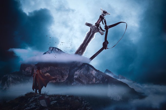 A cloaked figure stands on a misty mountain peak gazing up at a colossal sword, "Sword of Destiny," embedded in a stone amid dramatic clouds — capturing the legendary, mythic grandeur inspired by *King Arthur: Legend of the Sword (2017)*.