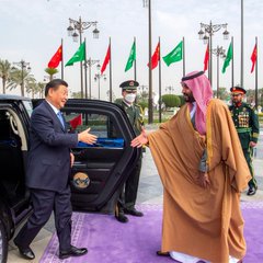A man in a suit steps out of a black car and shakes hands with Saudi Crown Prince Mohammed bin Salman, with Saudi and Chinese flags visible in the background. The image suggests a diplomatic meeting between Chinese and Saudi leaders, but the caption claims Saudi Arabia is exiting a China-led digital currency project to reinforce US Dollar dominance in oil trade.