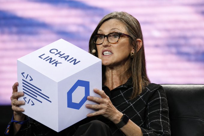 Cathie Wood of Ark Invest holds a large white cube labeled 'CHAIN LINK' with the Chainlink cryptocurrency logo at an investment conference.